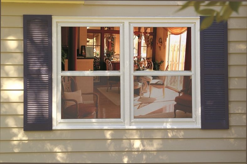 White double-hung window with dark shutters on a siding-clad home