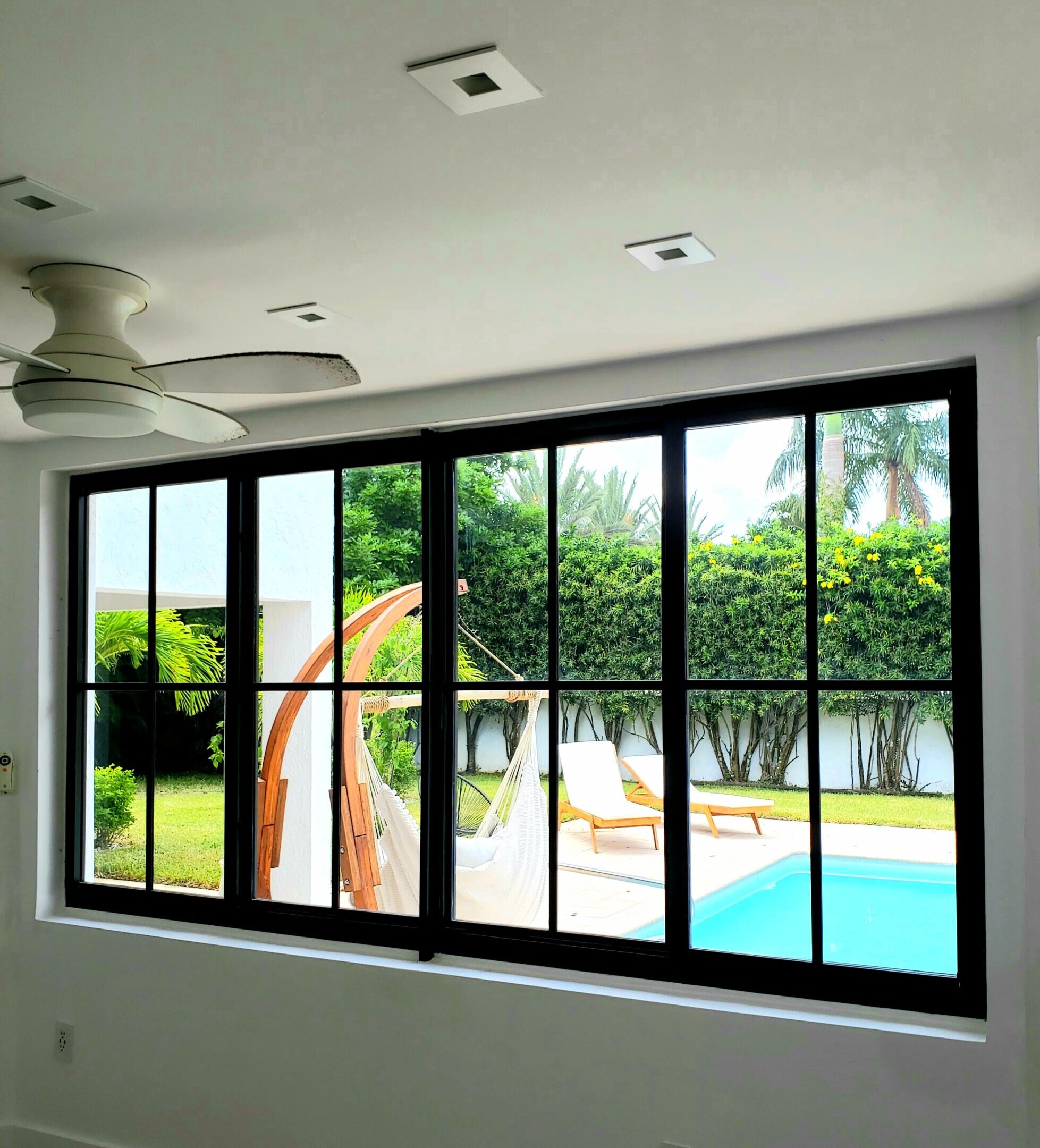 Black-framed horizontal rolling impact window overlooking a backyard pool