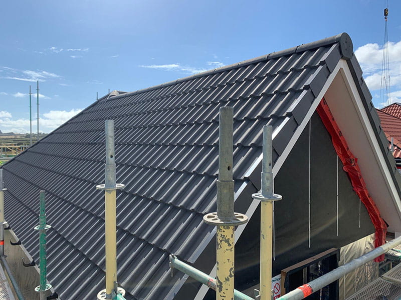 Dark metal tile roof being installed with scaffolding in place